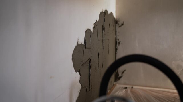Tiler's hand using a notched trowel to apply grey mortar adhesive onto a wall, preparing for the ceramic tile installation on a kitchen backsplash during a home improvement project