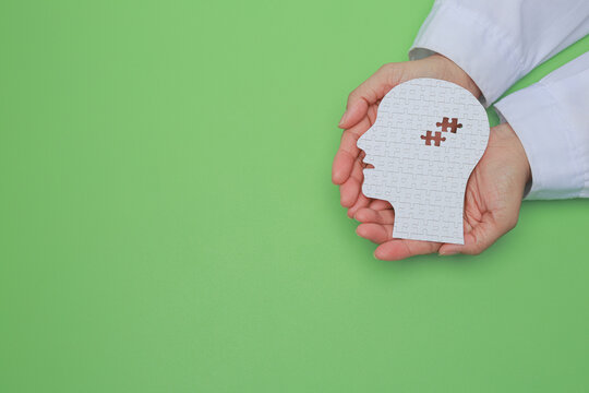 Compassionate doctor hand holding paper head puzzle showing brain mental health care concept with gentle hope for emotional wellness on green background