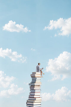 Student studying on top of tall book stack reaching into clouds. Concept of academic growth, study motivation and continuous educational progress.