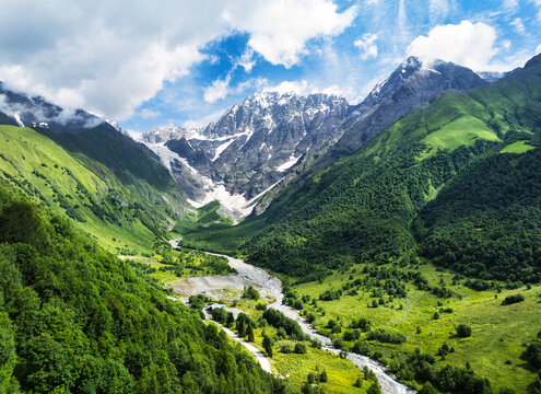 Green forest aerial view with background snow capped mountain. Koruldashi glacier at Racha-Lechkhumi and Lower Svaneti, Georgia