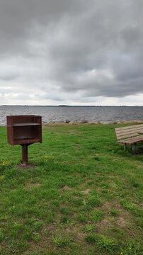 Hals, Denmark &ndash; August 26, 2026: Picnic table, benches, and a barbecue grill along the waterfront of the Limfjord on an overcast day