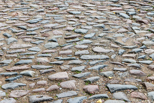 Old cobblestone background street pavement texture with natural stones and sand.