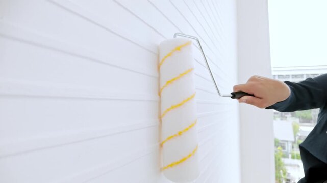 Hand using a paint roller to coat a white paneled wall, applying smooth coverage during a home DIY painting project.