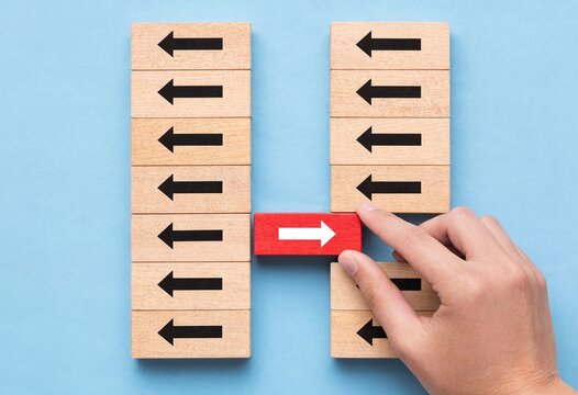 A person placing a unique red block with a white arrow in the opposite direction against a group of wooden blocks pointing left