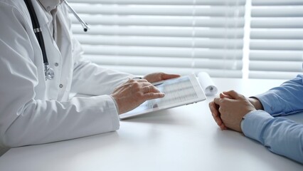 Doctor reviews digital health records with patient on tablet, explaining diagnosis and treatment...