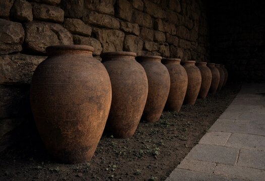 Row of traditional clay qvevri wine jars standing along an old stone wall in Georgia