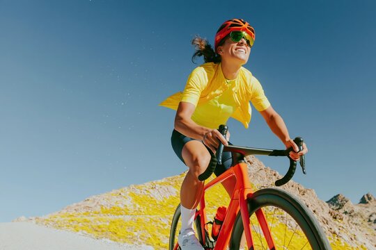 Athletic woman riding a streamlined road bicycle on a mountain route, featuring wind-tossed hair and a vibrant palette for endurance cycling and outdoor fitness