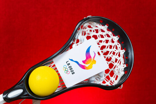 ZhongShan GuangDong China-September 5 2026: Lacrosse stick holding yellow ball and LA 2028 Olympics branded badge against red textured background.