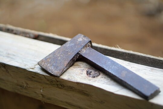 Traditional old iron axe lying on a wooden board at a woodworking area.