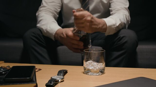 Caucasian middle aged businessman pouring whiskey from decanter into glass with ice and drinking. Footage suitable for corporate burnout campaigns and addiction recovery commercials