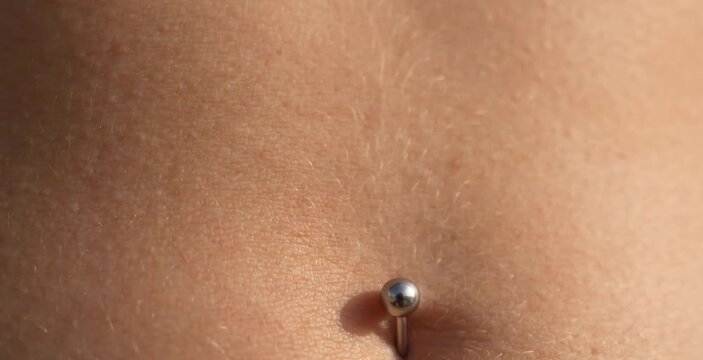 Macro Close Up of Classic Silver Ball Barbell Navel Belly Button Piercing in Sunlight
