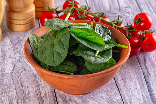 Fresh spinach leaves in terracotta bowl with cherry tomatoes on vine and wooden salt pepper shakers on rustic gray wood table