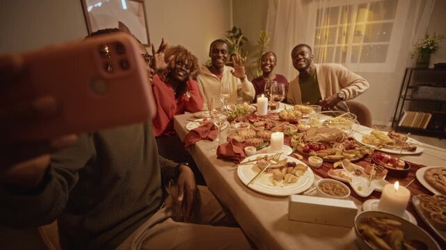 Portrait of young adult African American friends waving at smartphone camera during Thanksgiving dinner. Perfect for holiday marketing campaigns and social media promos