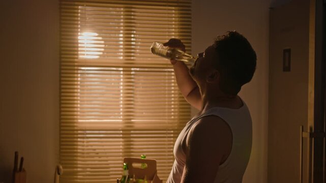 Middle aged Caucasian man drinking water from bottle and rubbing wet face in kitchen. Clip suitable for substance abuse prevention campaigns, mental health awareness and addiction recovery ads