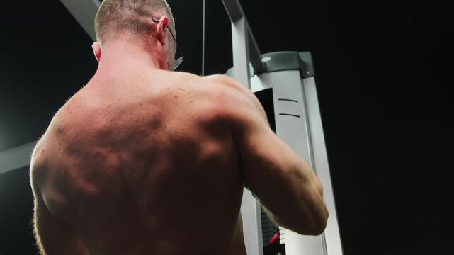 Man performs close grip pulldown on cable machine during gym training. Athlete pulls handle downward keeping back muscles engaged with control