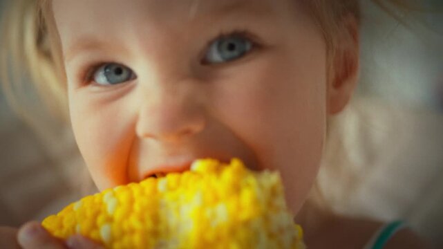 In home kitchen during the harvest season, a small child girl holds a kachan and eats boiled corn, the kernels appearing ripe and steam rising, captured in a close-up view of the simple meal, concept