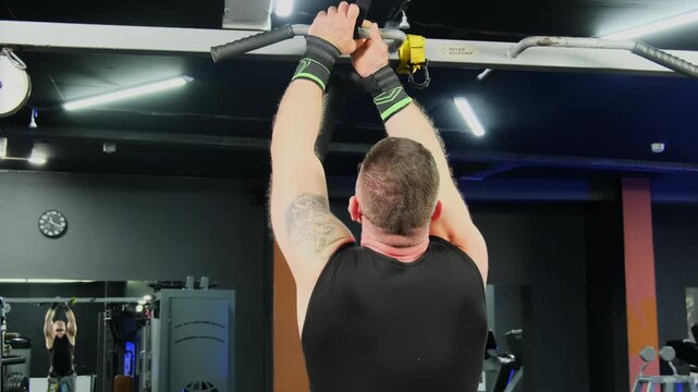 Fitted man wraps training bandage around pull up bar before exercise. Athlete secures wrist support firmly preparing grip for workout