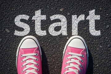 Obraz premium Top view of pink sneakers on black asphalt road. White text says start on ground. Woman stands at starting line ready to begin journey race. Concept of new beginning, motivation, personal goal career