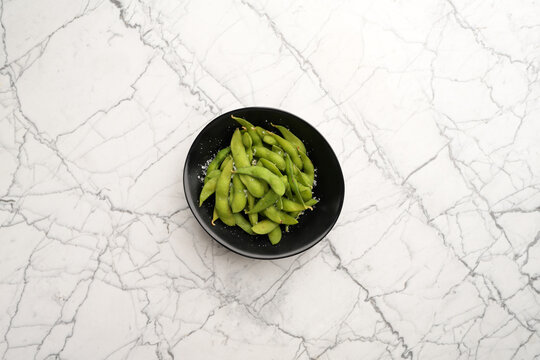Steamed edamame beans sprinkled with sea salt in black bowl flat lay