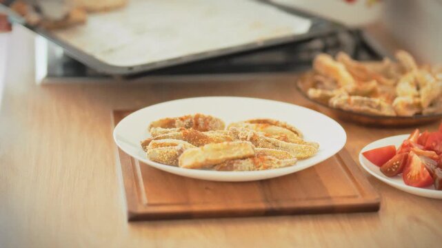 Transferring baked eggplant from tray to plate using tongs. A housewife prepares healthy oven-baked food at home in daylight. Concept of homemade cooking and natural healthy meal