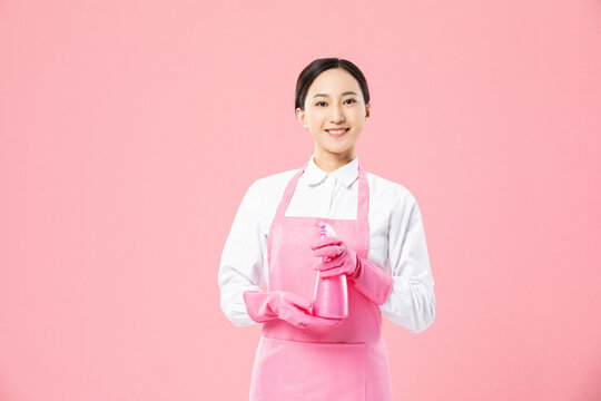 Smiling Asian woman in pink cleaning uniform with pink spray bottle