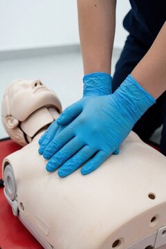 Hands in blue gloves practice chest compressions on CPR dummy during first aid training. Medical skills learning on mannequin for emergency response. Practicing lifesaving techniques in classroom