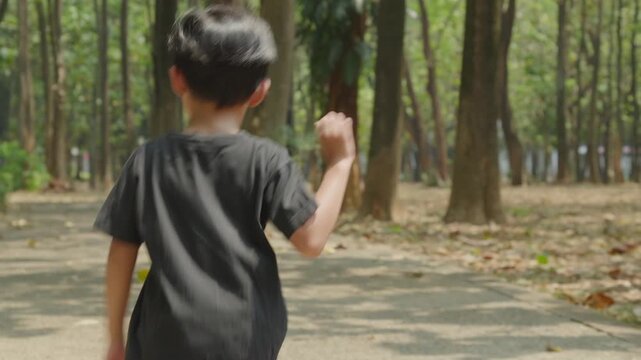 rear view of a young child running along a paved path through a tree lined park