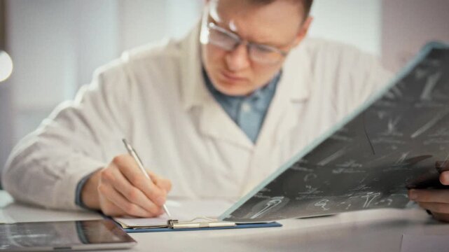 A doctor carefully fills out a medical record while examining an MRI printout of the injury, viewing multiple projections to plan an integrated fracture treatment in a bright office