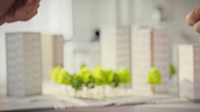 A female real estate agent hands over shiny keys to a male client in a bright office with three-dimensional models of apartment buildings in the background. Concept of property purchase completion