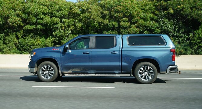 Newark, Delaware, U.S.A - Aug 29, 2026 - Blue Chevrolet Silverado Z71 with camper shell driving on highway beside dense green foliage and concrete barrier on highway I-95
