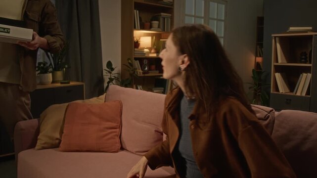 Caucasian young woman using smartphone receiving online shopping delivery parcels from her husband at home. Perfect for e-commerce, courier services, and tech marketing