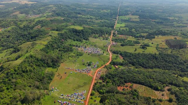 Rural rally campsite beside a long dirt road in Nueva Alborada, Paraguay, aerial panoramic pullback