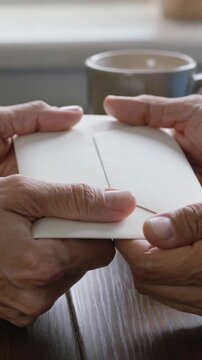 Vertical video: Coming from upper left, white envelope making four hands holding at table with mug