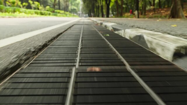 Low angle tracking shot along a roadside storm drain grate in a tree lined street