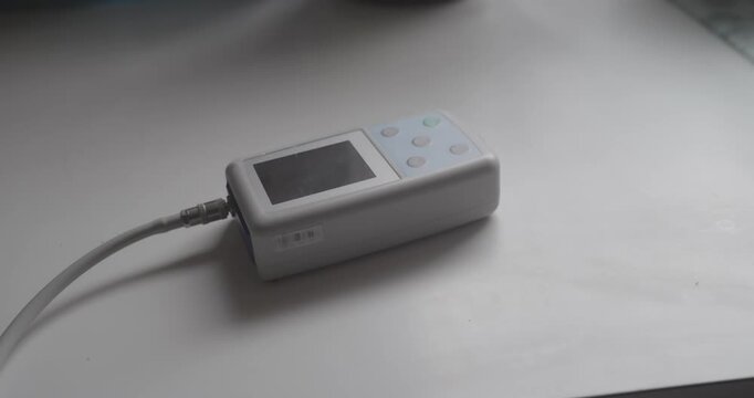 Home patient places a 24-hour ambulatory blood pressure Holter monitoring device onto a desktop surface. Represents remote patient monitoring RPM and digital home healthcare concepts.