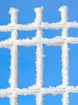 Gros plan d'un grillage gel&eacute; couvert de givre blanc, avec un ciel bleu en arri&egrave;re plan. Lignes couvertes de glace.