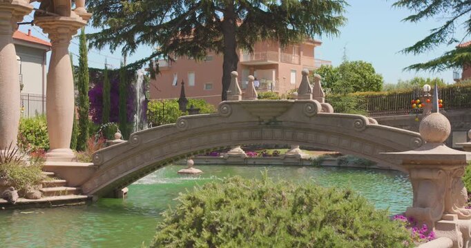 Stone arch bridge over pond with fountains in Villa Grock gardens, sunny day