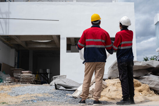 Construction engineers inspecting a residential building exterior, reviewing architectural plans, site progress, structural quality, and safety compliance before project completion.
