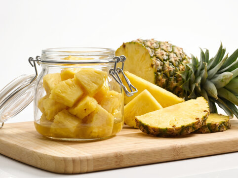 Glass jar filled with fresh pineapple chunks beside a whole cut pineapple on wood