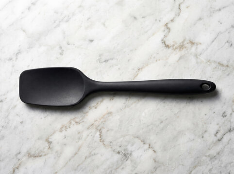 Flat lay of a modern black silicone cooking spatula on a white marble counter