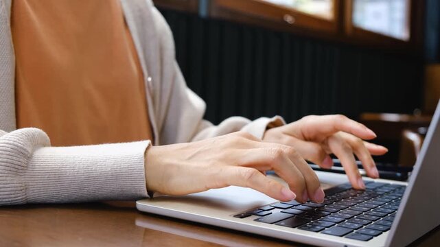 Close-up of a woman typing on a laptop at cafe. Representing remote work, technology, business and online work.