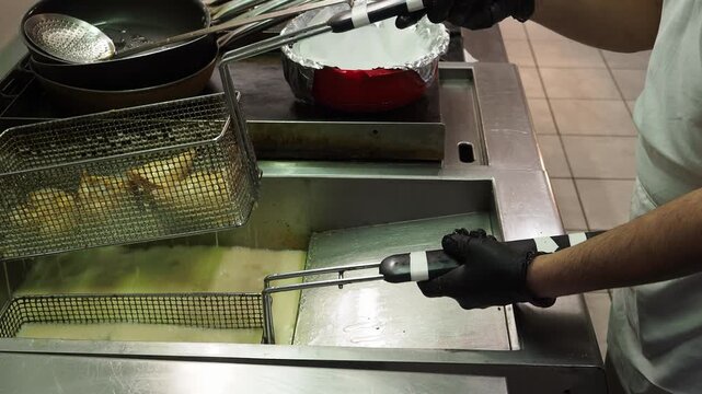 Samosas deep fry in hot oil inside a commercial fryer as a chef handles the basket during professional Indian food preparation, static close-up.
