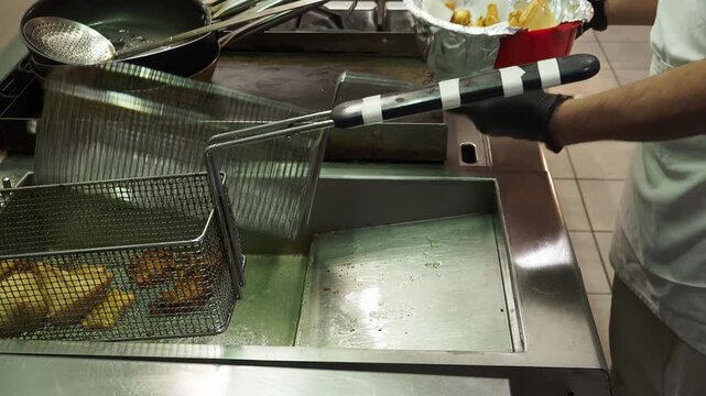 Chef transfers freshly fried samosas from a fryer basket onto paper to absorb excess oil during professional Indian food preparation, static close-up.