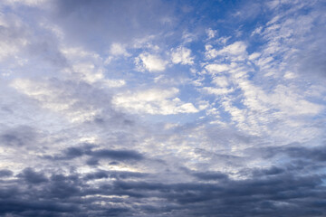 Fototapeta premium Bright blue daytime sky with soft white clouds,A wide-angle photograph of a serene blue sky filled with soft white and light grey cloud formations during the daytime. Bright natural sunlight filters 