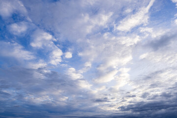 Fototapeta premium Bright blue daytime sky with soft white clouds,A wide-angle photograph of a serene blue sky filled with soft white and light grey cloud formations during the daytime. Bright natural sunlight filters 