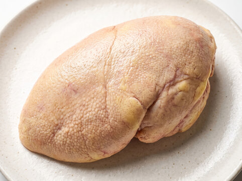 Fresh raw goose foie gras lobe resting on a light ceramic plate