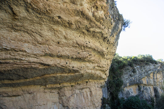 Layered limestone rock overhang and shelter seen from below against a bright sky