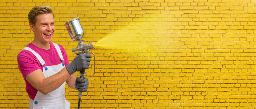 Man spraying yellow paint on brick wall with paint sprayer  