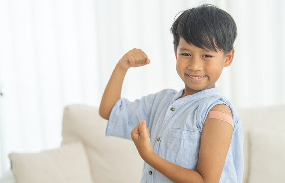 Asian boy strong pose with a raised fist after vaccination with bandage on arm, child health care, hospital service, influenza vaccine protection, covid prevention, pediatric safety immunity booster