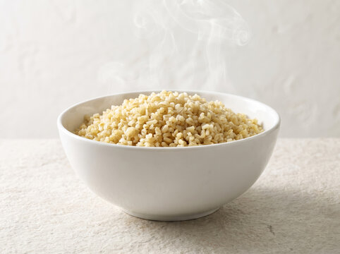 Steaming hot boiled brown bulgur groats served in a white bowl